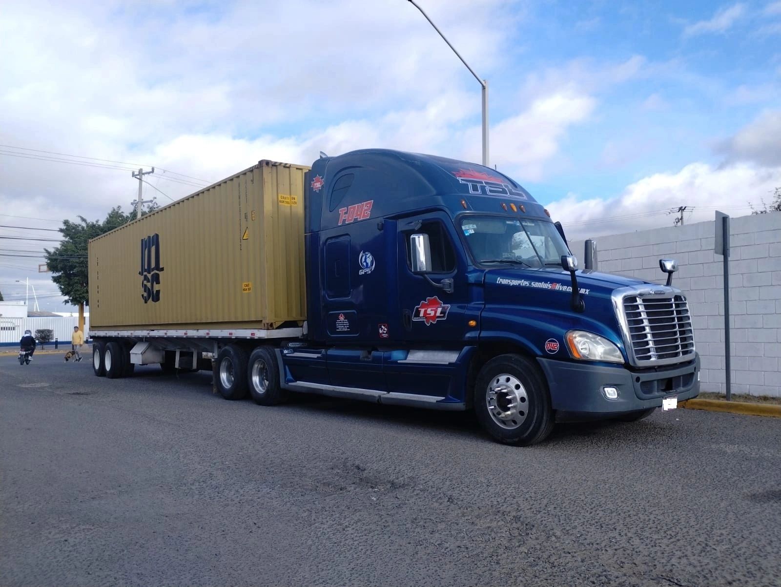 Tractocamión azul de TSL con contenedor amarillo en terminal de carga